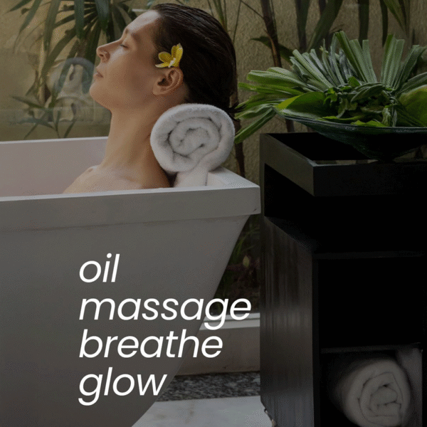 A woman relaxes in a white bathtub with her head resting on a rolled towel, a flower in her hair & surrounded by lush green plants. The text on the image reads: Z Secrets Hair Elixir, massage, breathe, glow.